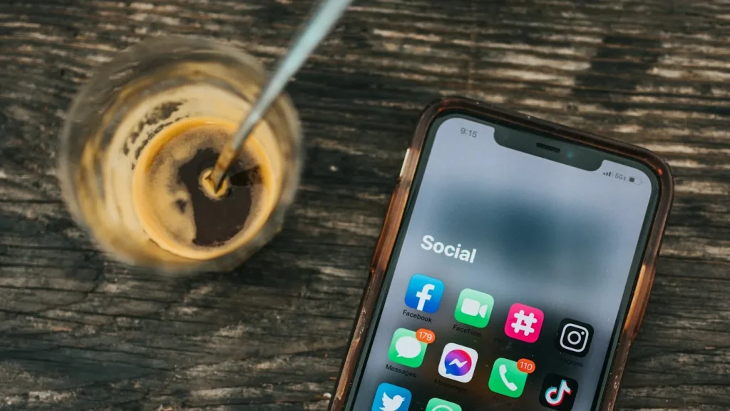 Smartphone displaying social media apps beside a glass of coffee